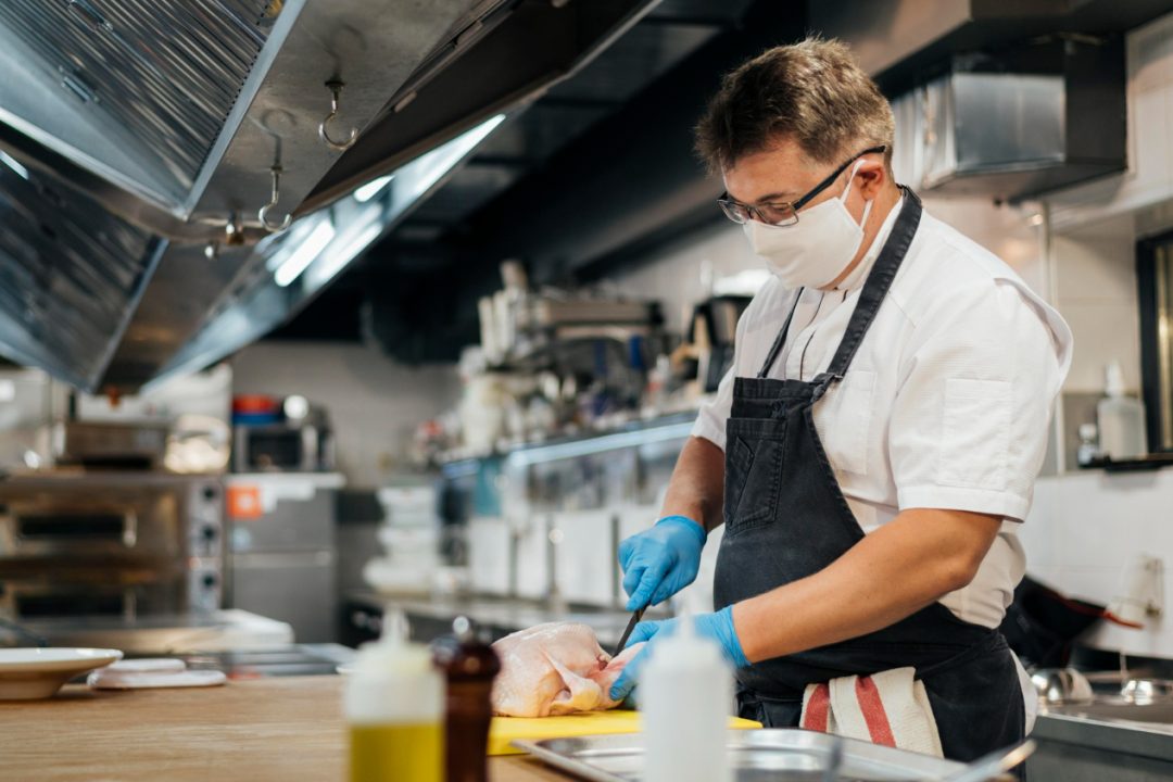 side-view-male-chef-with-mask-cutting-chicken
