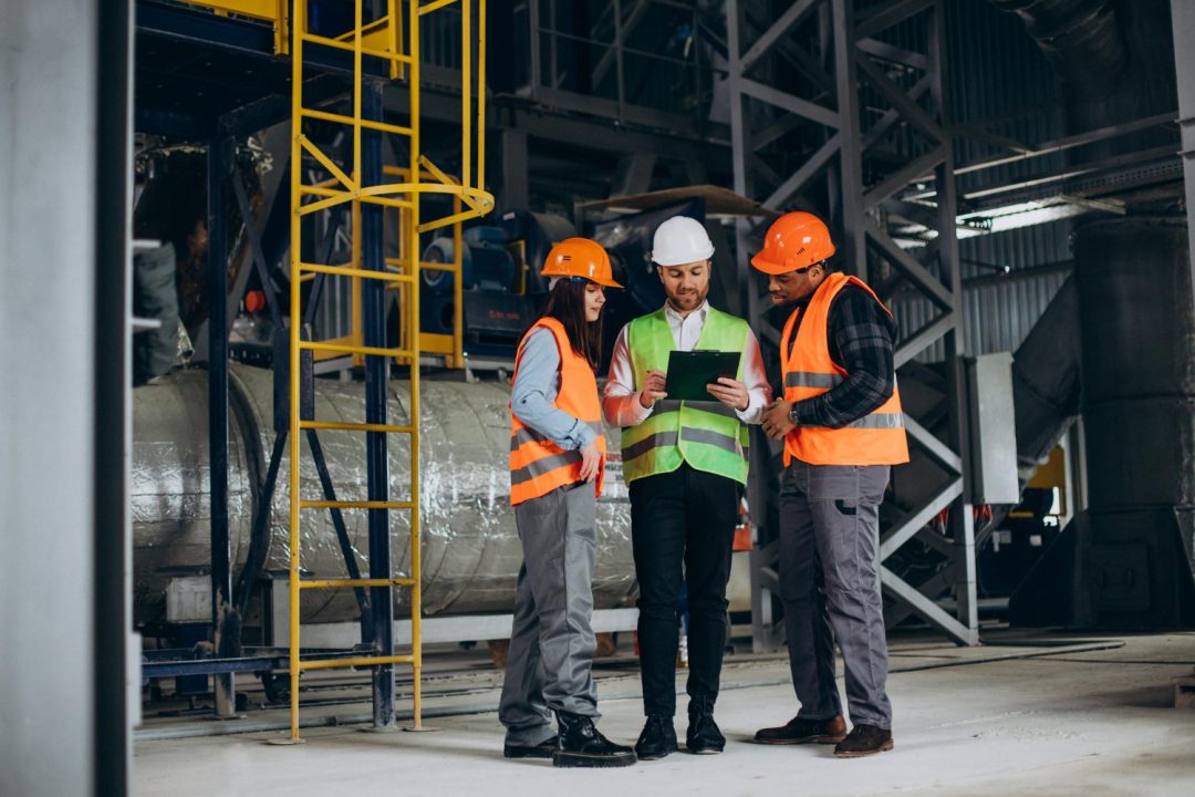three-factory-workers-safety-hats-discussing-manufacture-plan